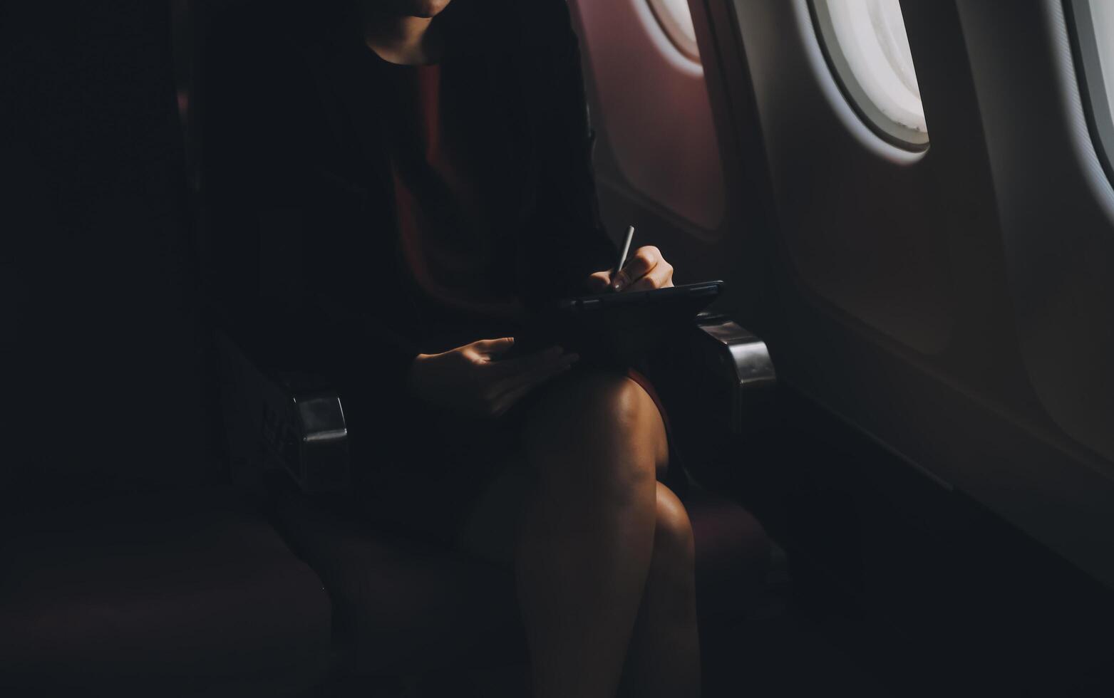 Blonde female tourist checking incoming notification on smartphone sitting on seat of airplane with netbook.Young businesswoman share media from telephone on laptop computer during plane flight photo