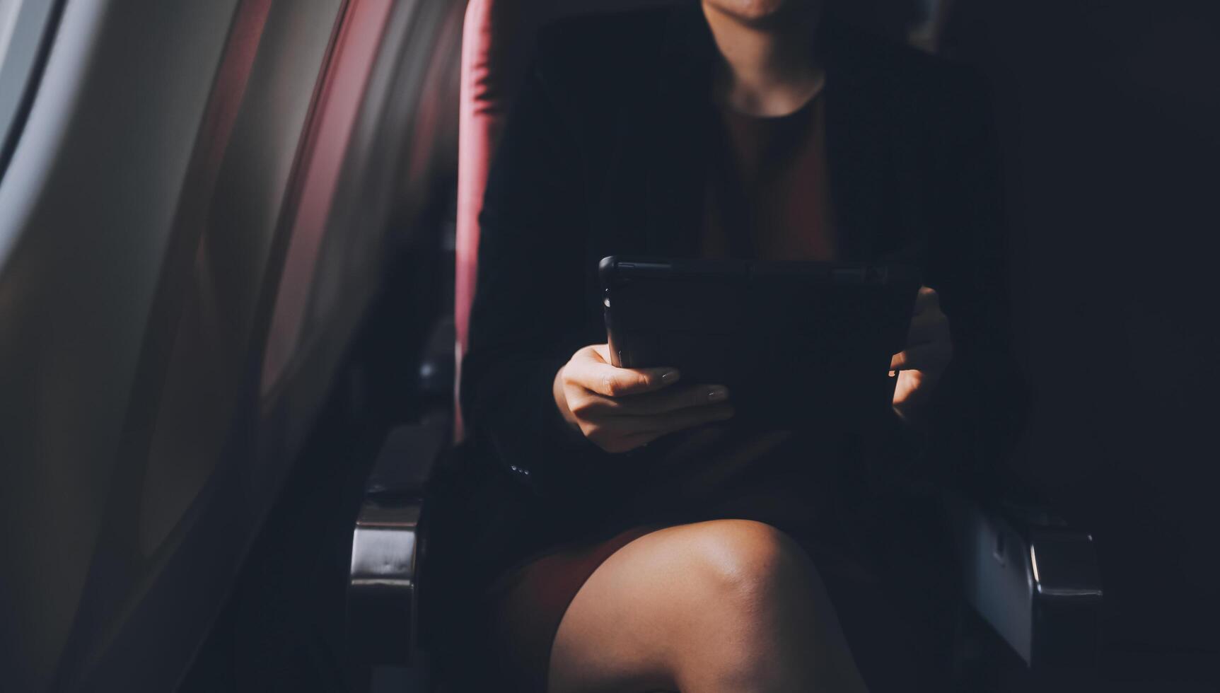 Blonde female tourist checking incoming notification on smartphone sitting on seat of airplane with netbook.Young businesswoman share media from telephone on laptop computer during plane flight photo