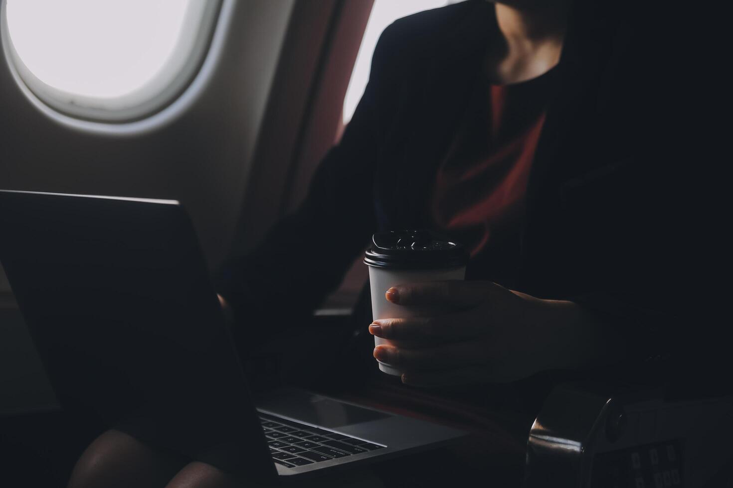 Blonde female tourist checking incoming notification on smartphone sitting on seat of airplane with netbook.Young businesswoman share media from telephone on laptop computer during plane flight photo
