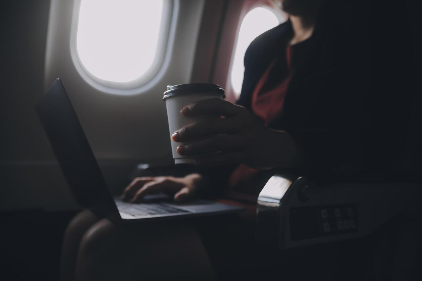 Blonde female tourist checking incoming notification on smartphone sitting on seat of airplane with netbook.Young businesswoman share media from telephone on laptop computer during plane flight photo