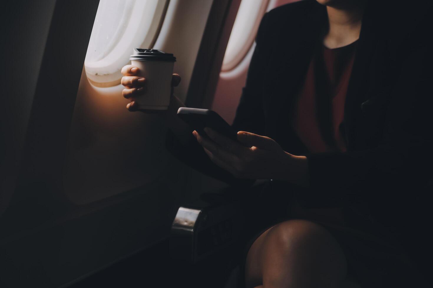 Blonde female tourist checking incoming notification on smartphone sitting on seat of airplane with netbook.Young businesswoman share media from telephone on laptop computer during plane flight photo