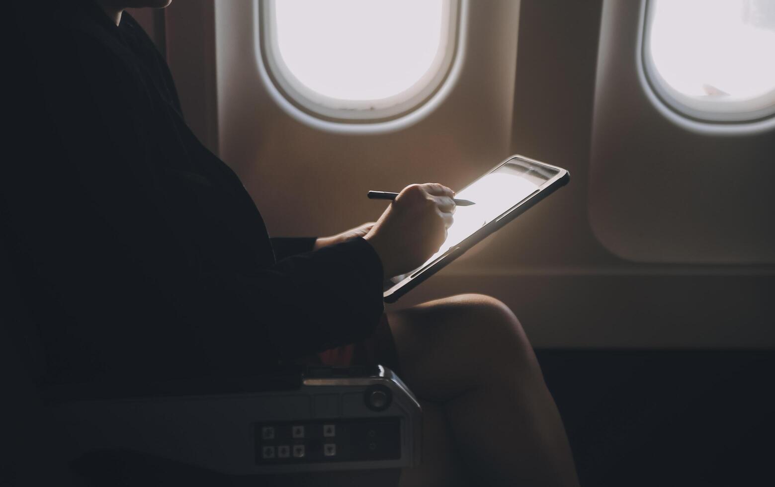 Blonde female tourist checking incoming notification on smartphone sitting on seat of airplane with netbook.Young businesswoman share media from telephone on laptop computer during plane flight photo