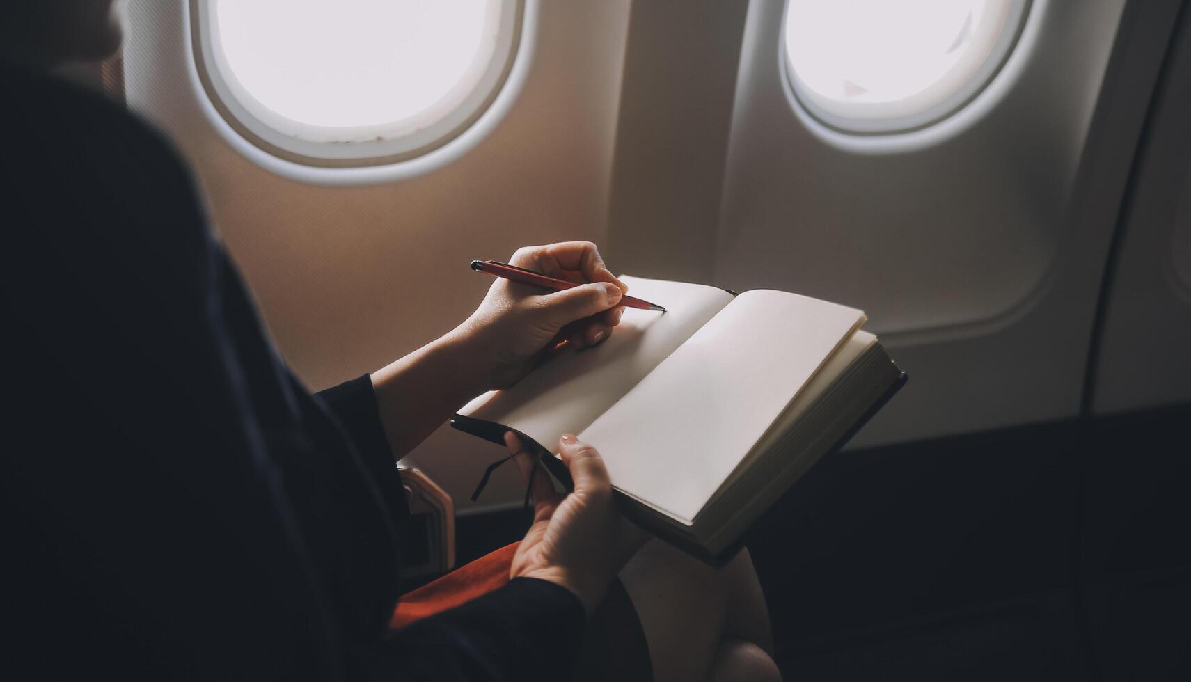 Blonde female tourist checking incoming notification on smartphone sitting on seat of airplane with netbook.Young businesswoman share media from telephone on laptop computer during plane flight photo