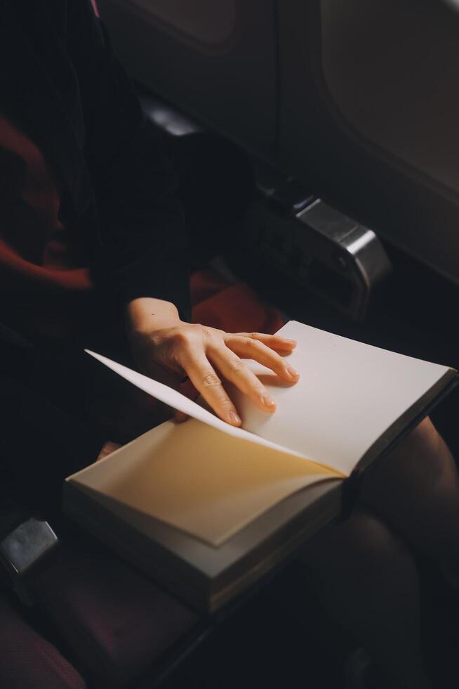 Blonde female tourist checking incoming notification on smartphone sitting on seat of airplane with netbook.Young businesswoman share media from telephone on laptop computer during plane flight photo