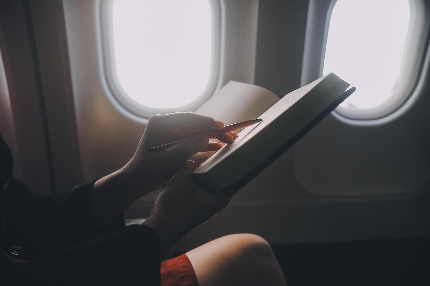 Blonde female tourist checking incoming notification on smartphone sitting on seat of airplane with netbook.Young businesswoman share media from telephone on laptop computer during plane flight photo