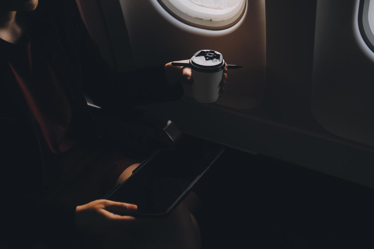 Blonde female tourist checking incoming notification on smartphone sitting on seat of airplane with netbook.Young businesswoman share media from telephone on laptop computer during plane flight photo
