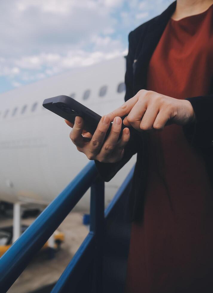 Young asian woman in international airport, using mobile smartphone and checking flight at the flight information board photo