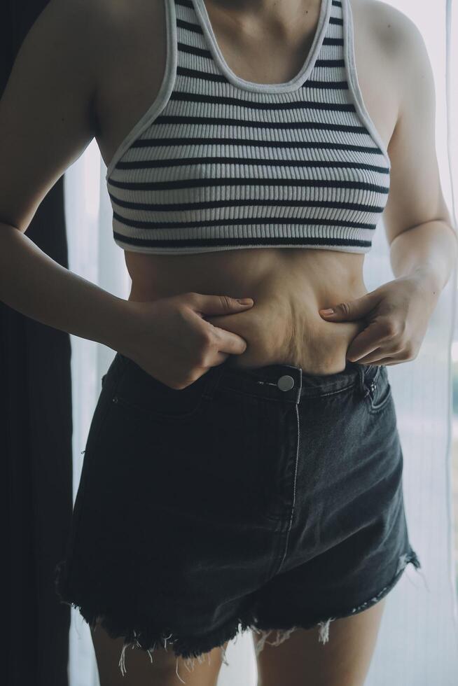Women body fat belly. Obese woman hand holding excessive belly fat. diet lifestyle concept to reduce belly and shape up healthy stomach muscle. photo