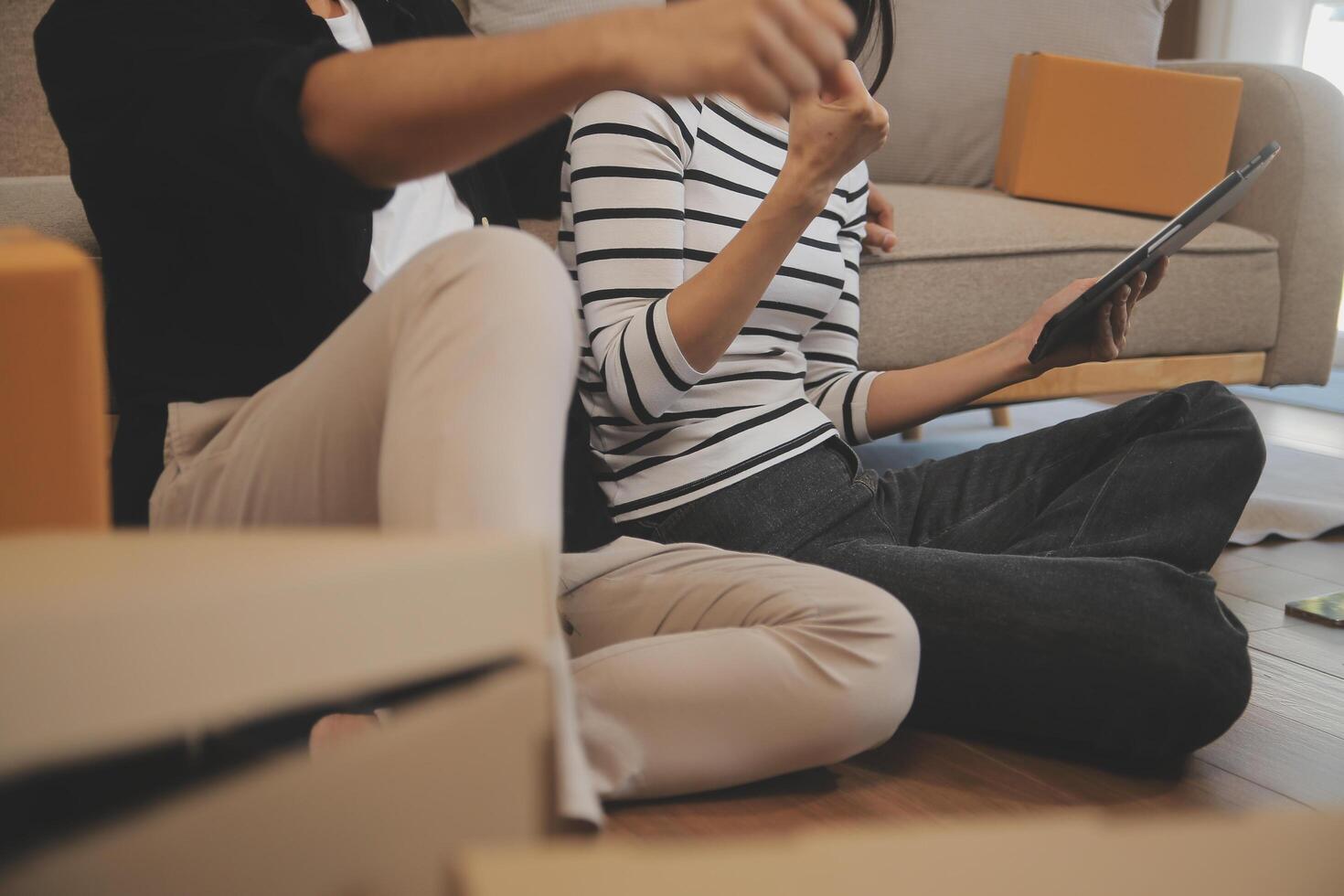 Two Asian blogger showing clothes in front of the camera to recording vlog video live streaming at her shop. Online Shopping Cart notion. on sofa at home photo