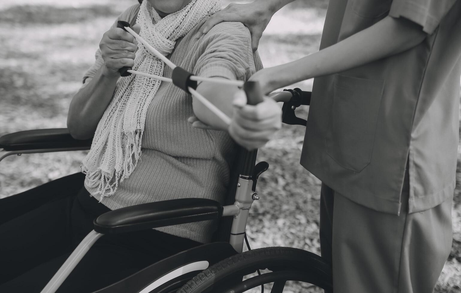 Young nurse or physiotherapist in scrubs helping a happy retired old woman do fitness exercises with light weight dumbbells at home. Concept of physiotherapy for seniors photo