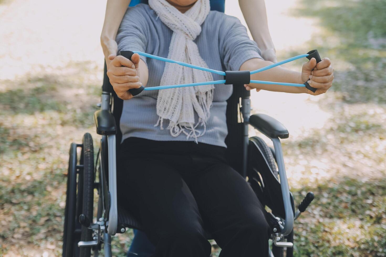 Young nurse or physiotherapist in scrubs helping a happy retired old woman do fitness exercises with light weight dumbbells at home. Concept of physiotherapy for seniors photo