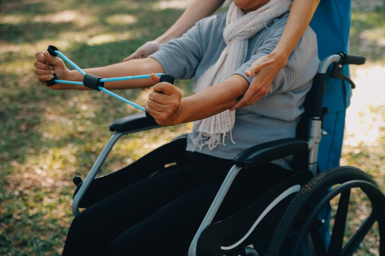 Young nurse or physiotherapist in scrubs helping a happy retired old woman do fitness exercises with light weight dumbbells at home. Concept of physiotherapy for seniors photo