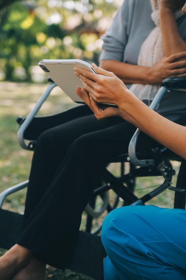 Elderly asian senior woman on wheelchair with Asian careful caregiver and encourage patient, walking in garden. with care from a caregiver and senior health insurance in sun light photo