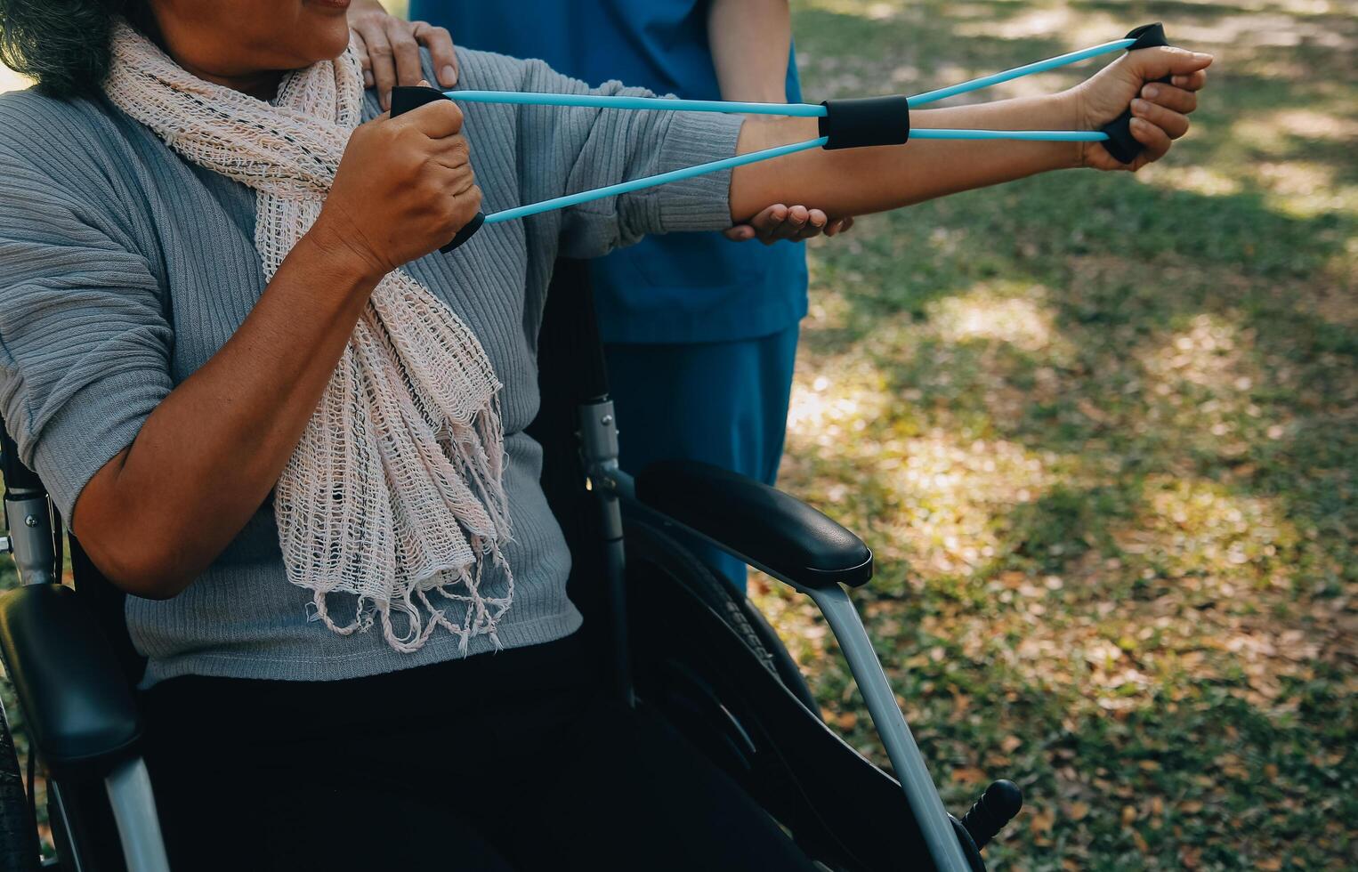 Young nurse or physiotherapist in scrubs helping a happy retired old woman do fitness exercises with light weight dumbbells at home. Concept of physiotherapy for seniors photo