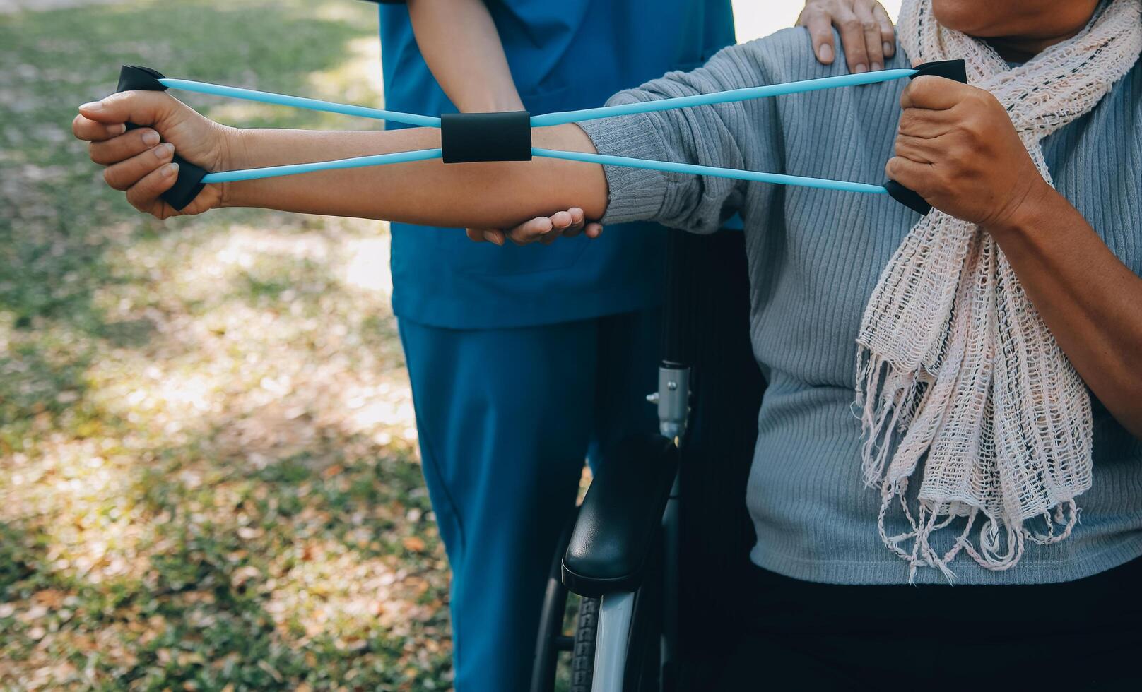 Young nurse or physiotherapist in scrubs helping a happy retired old woman do fitness exercises with light weight dumbbells at home. Concept of physiotherapy for seniors photo