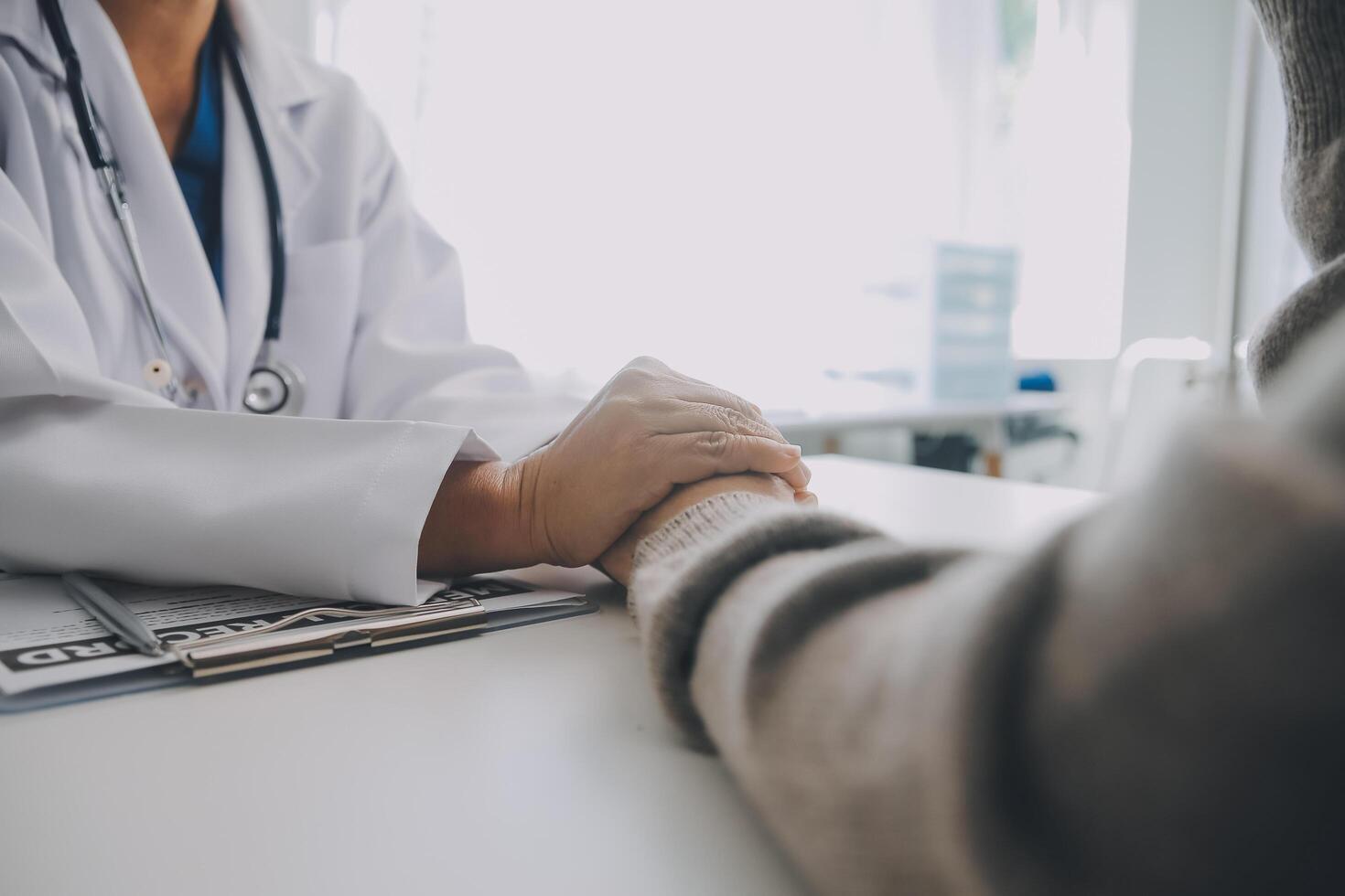 Doctor and patient sitting near each other at the table in clinic office. The focus is on female physician's hands reassuring woman, only hands, close up. Medicine concept photo