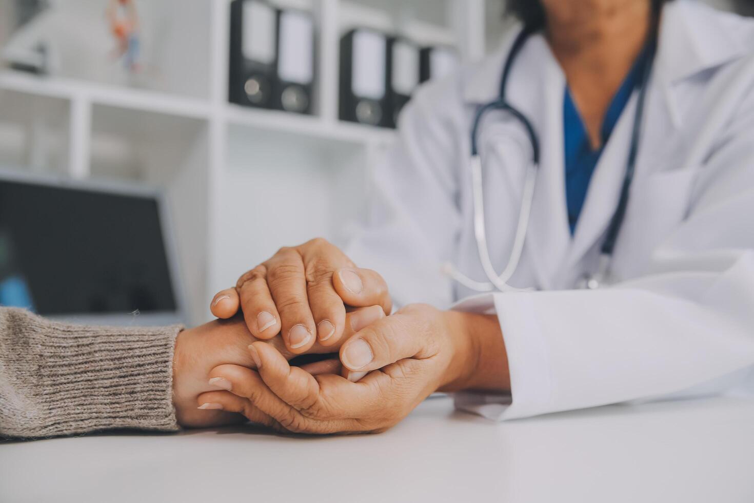 Doctor and patient sitting near each other at the table in clinic office. The focus is on female physician's hands reassuring woman, only hands, close up. Medicine concept photo