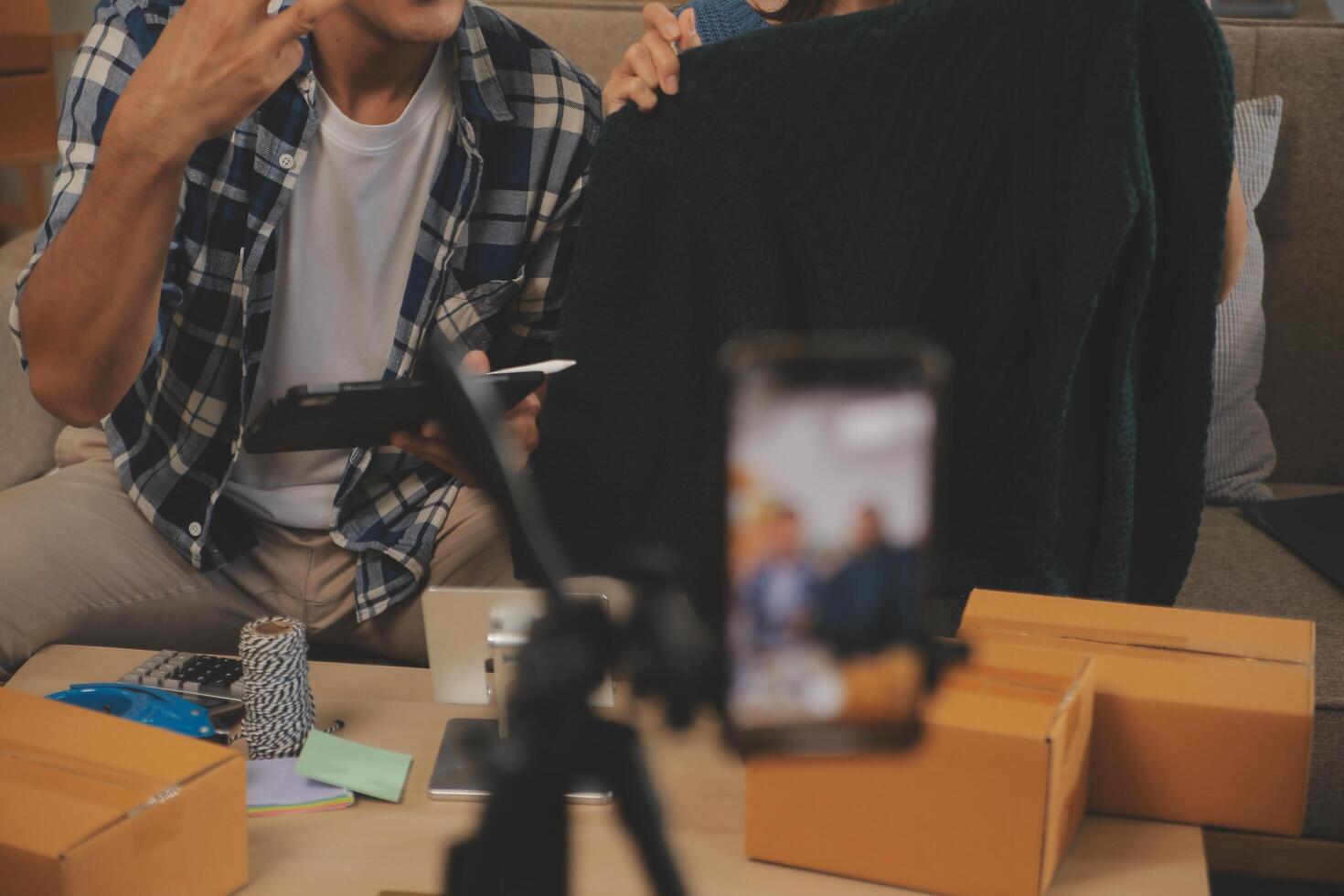 Two Asian blogger showing clothes in front of the camera to recording vlog video live streaming at her shop. Online Shopping Cart notion. on sofa at home photo