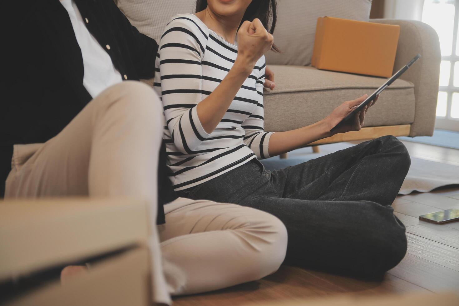 Two Asian blogger showing clothes in front of the camera to recording vlog video live streaming at her shop. Online Shopping Cart notion. on sofa at home photo