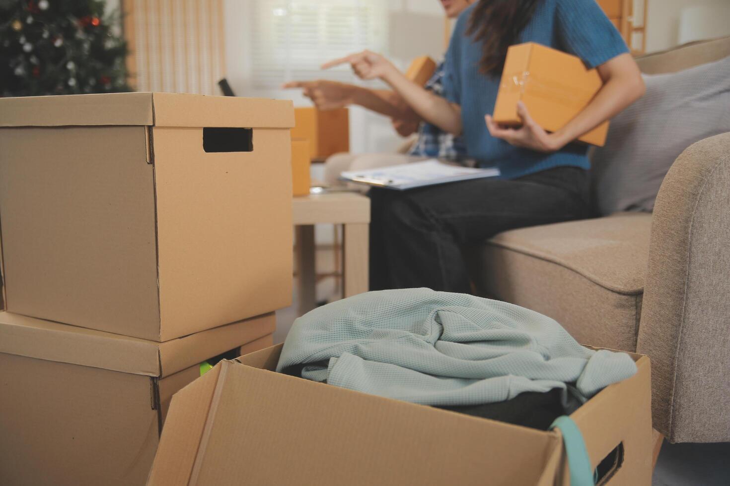 Two Asian blogger showing clothes in front of the camera to recording vlog video live streaming at her shop. Online Shopping Cart notion. on sofa at home photo