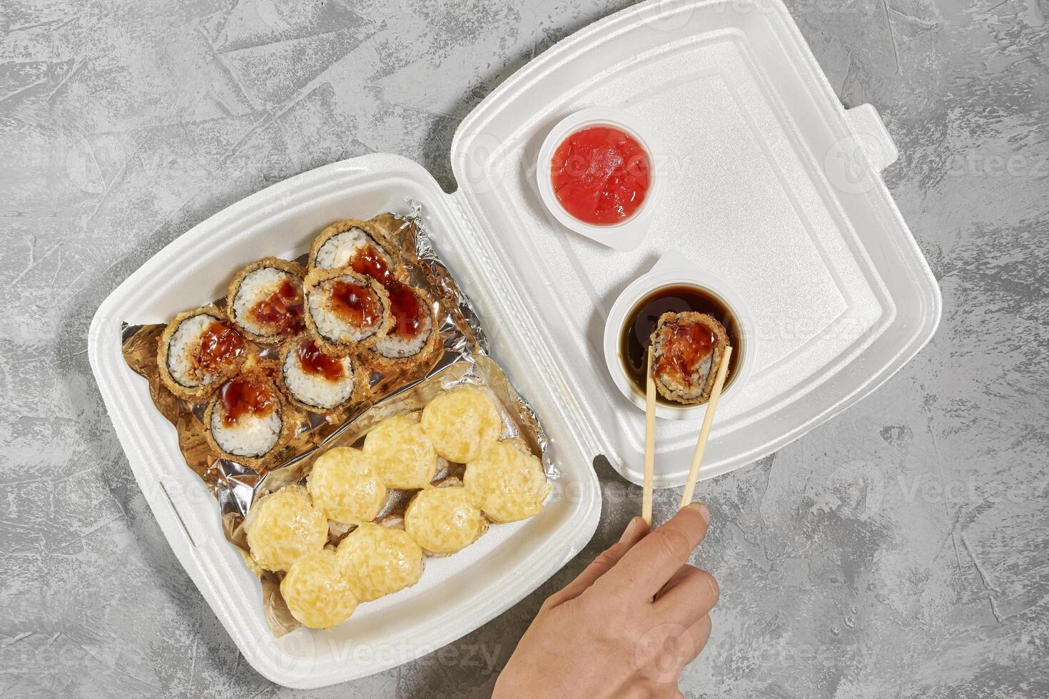 deliciosos rollos de sushi en cajas de plástico desechables. la mano toma un rollo con palillos. concepto de servicio de entrega de alimentos, apilamiento plano foto