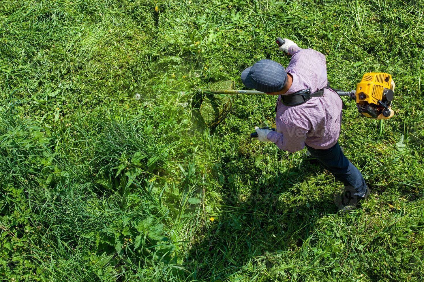 lawnmower man with string trimmer trimming grass at sunny day photo