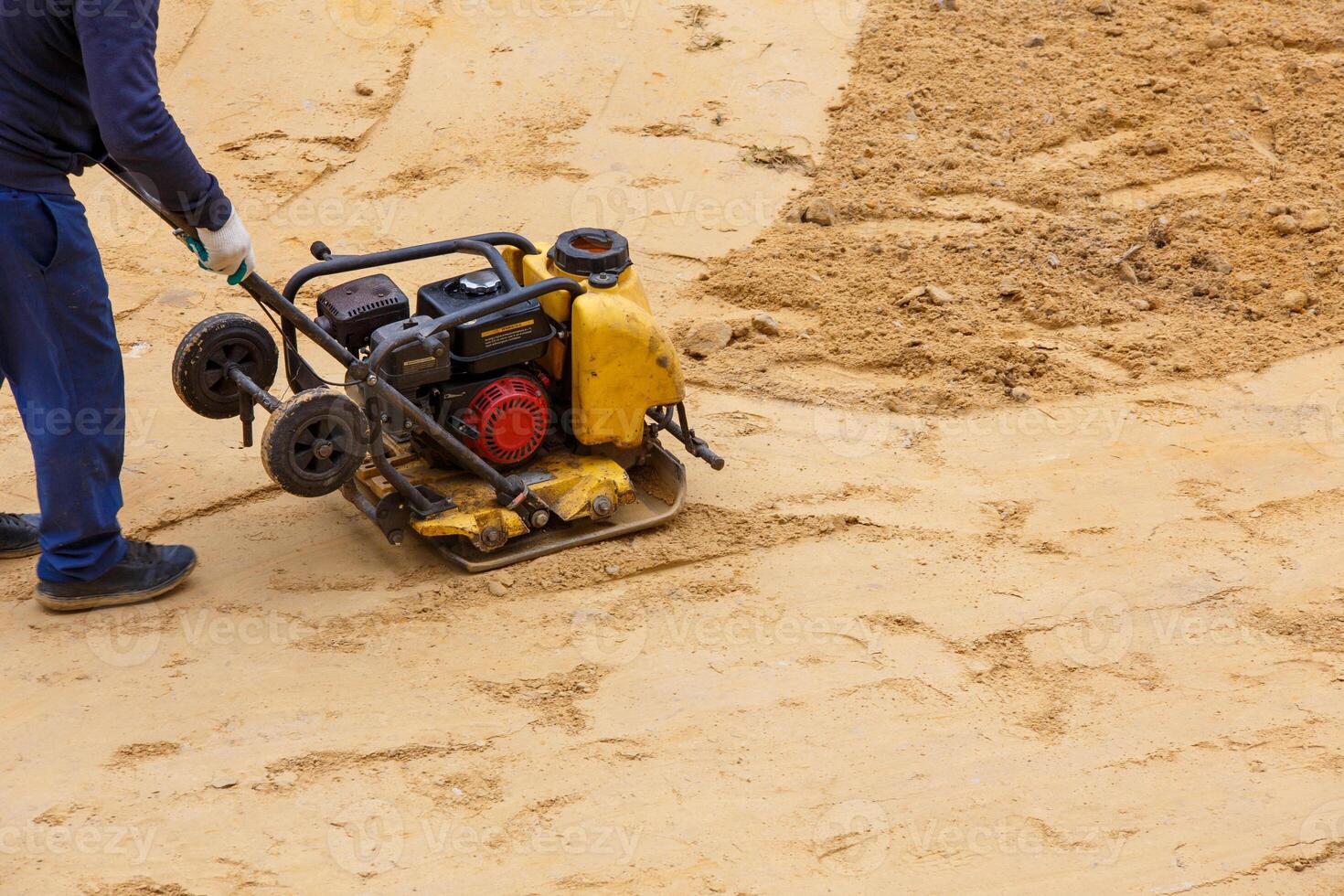 Worker using vibratory plate compactor for compaction sand during path construction. photo
