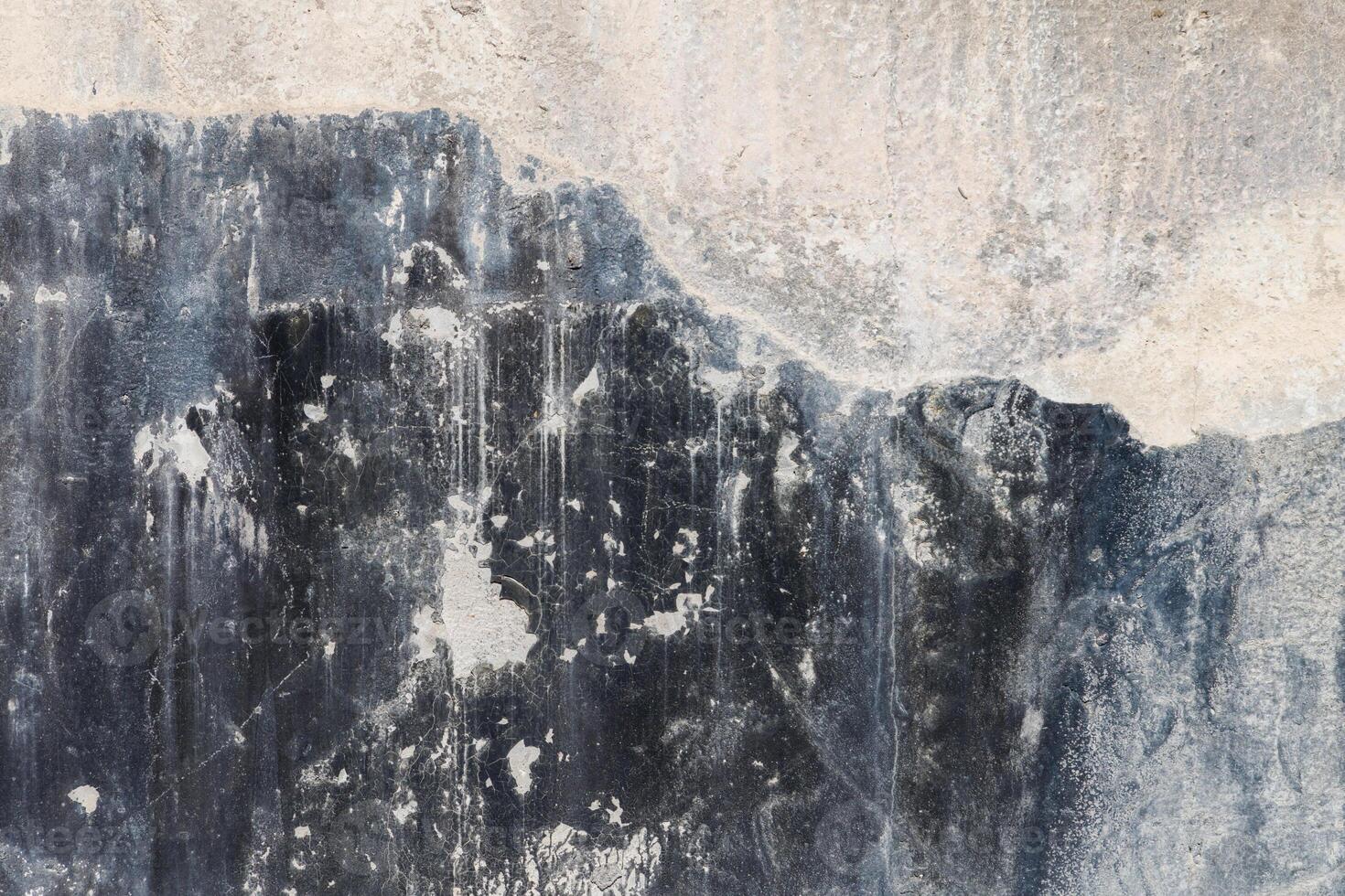 old concrete wall with black paint leftovers covered with whitewash stains, full-frame background and texture photo