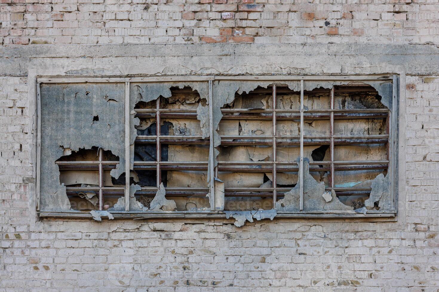 old window covered with torn ruberoid material and old wooden planks on white brick wall of an abandoned building photo