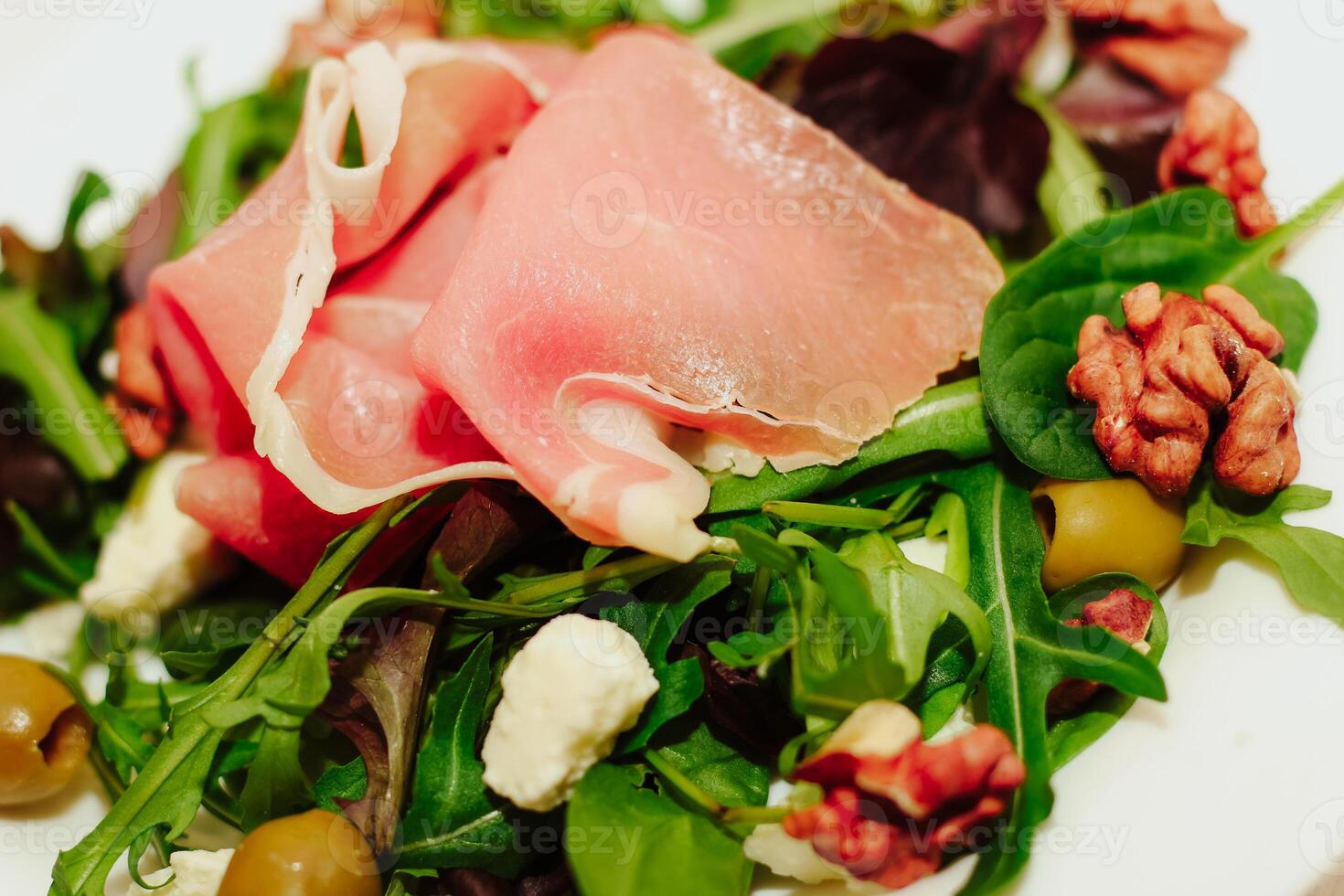 Salad with herbs, arugula, prosciutto, cheese, green olives and nuts. photo