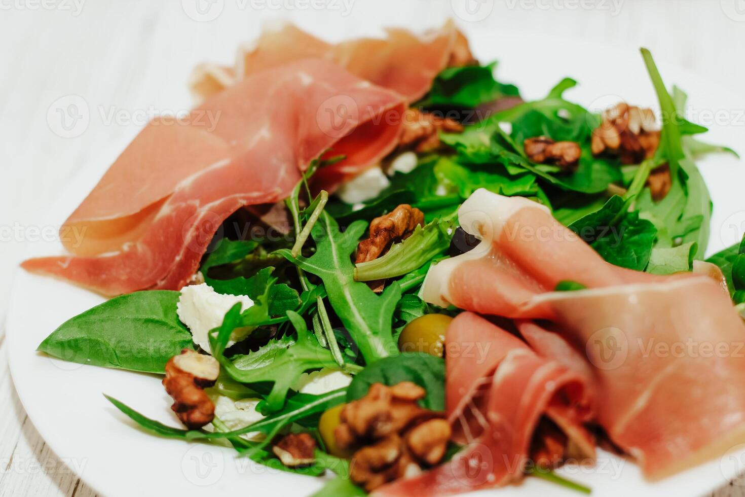 Salad with herbs, arugula, prosciutto, cheese, green olives and nuts. photo
