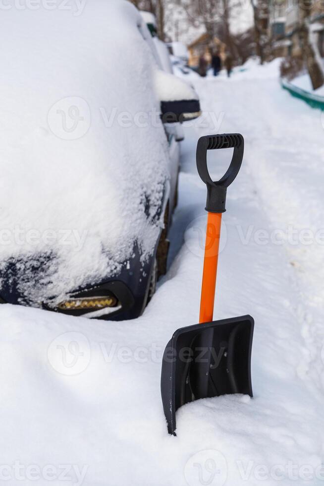 Plastic snow shovel in front of snow-covered car at winter morning photo