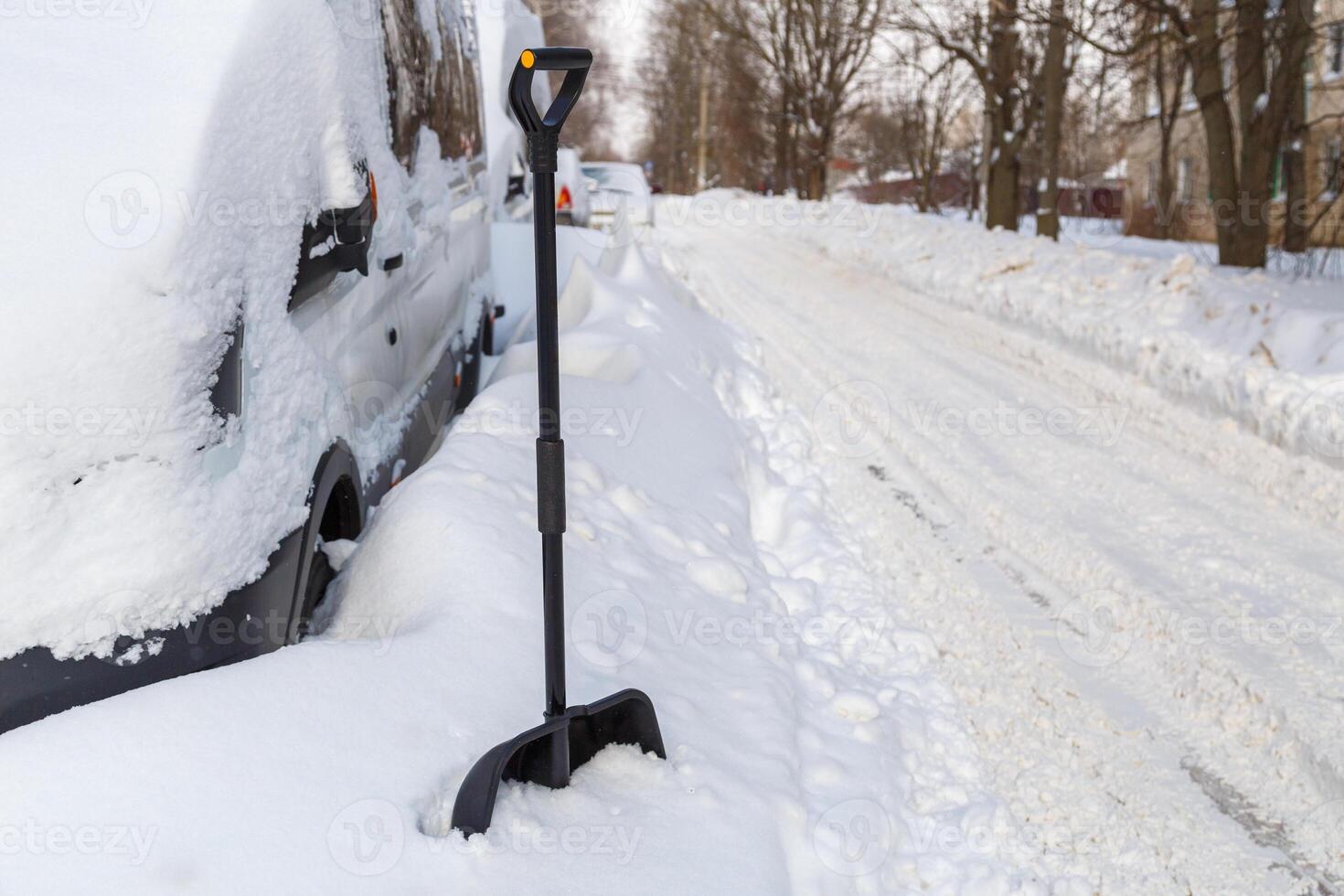 Plastic snow shovel in front of snow-covered minivan at sunny winter morning photo