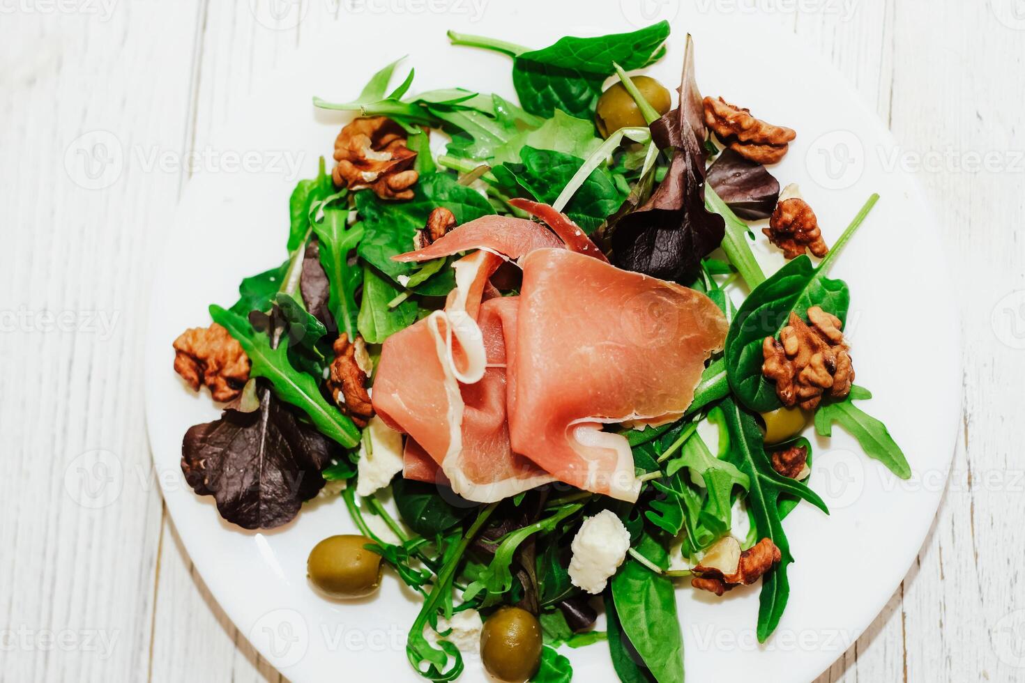 Salad with herbs, arugula, prosciutto, cheese, green olives and nuts. photo