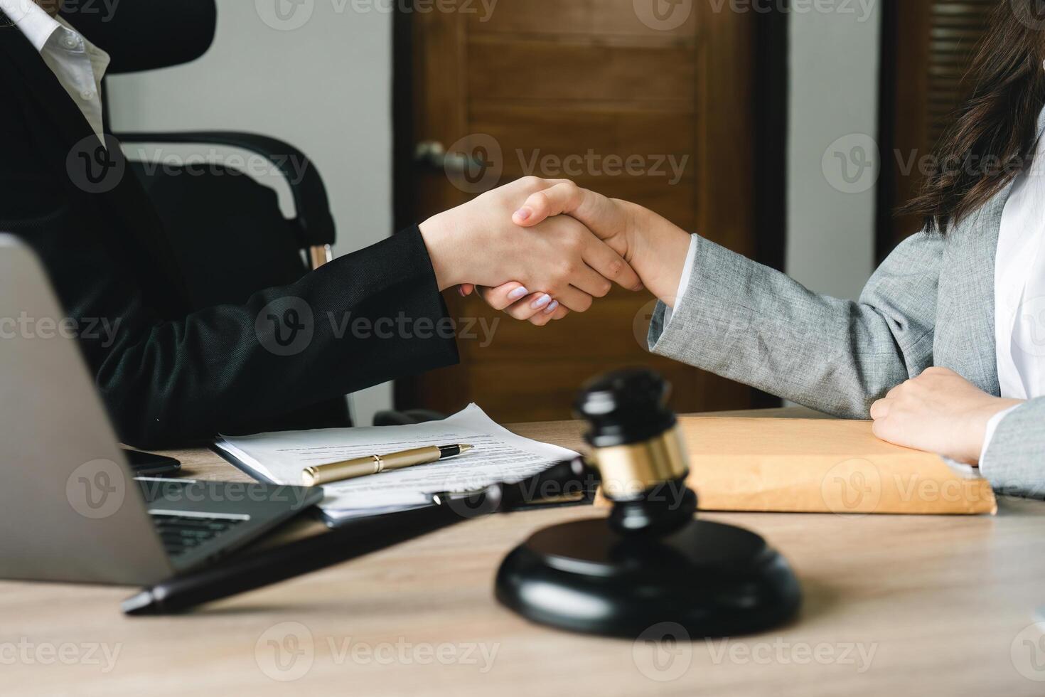 Gavel Justice hammer on wooden table with judge and client shaking hands after adviced in background at courtroom, lawyer service concept photo