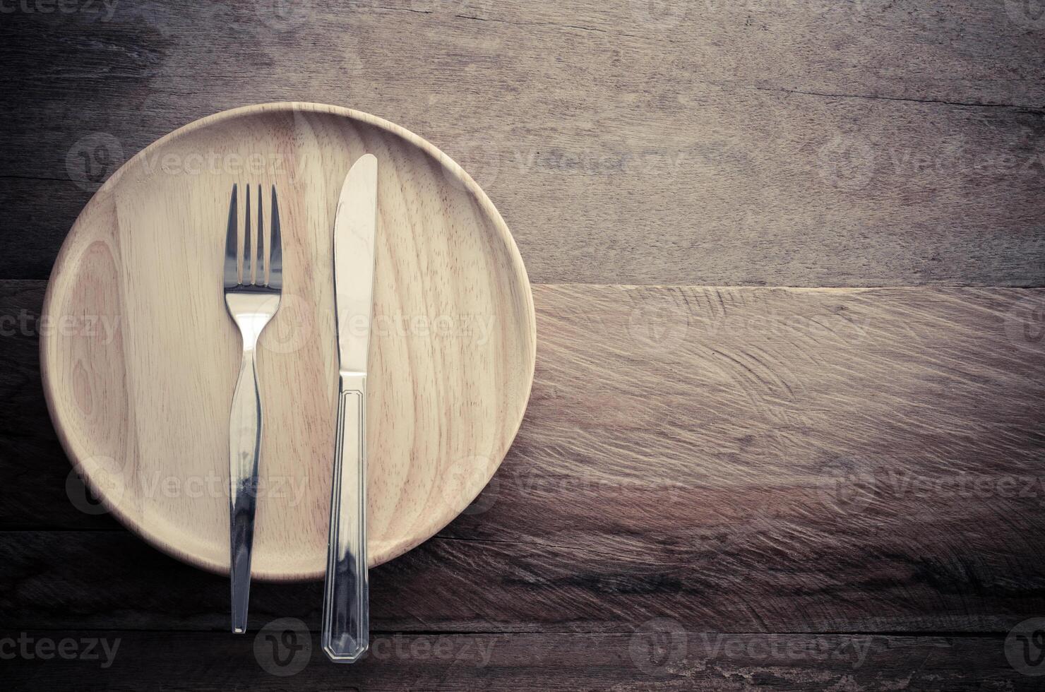 Knife and fork on wood plate placed on a wooden table - still life. photo