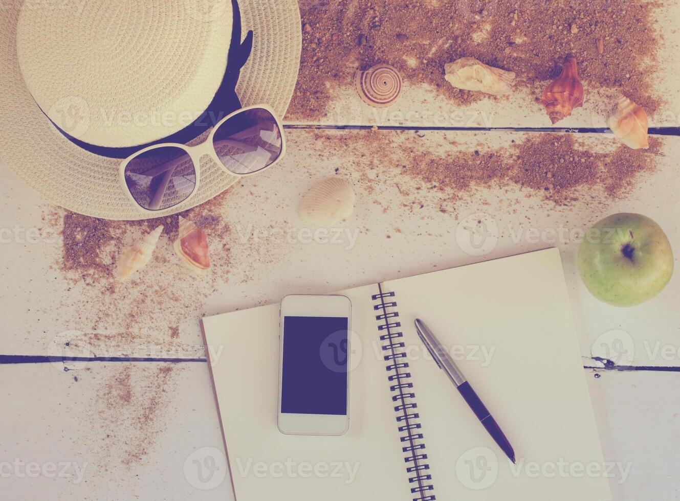 Travel accessories, hats, sunglasses, notebook, pen, phone, shell, placed on a wooden floor photo
