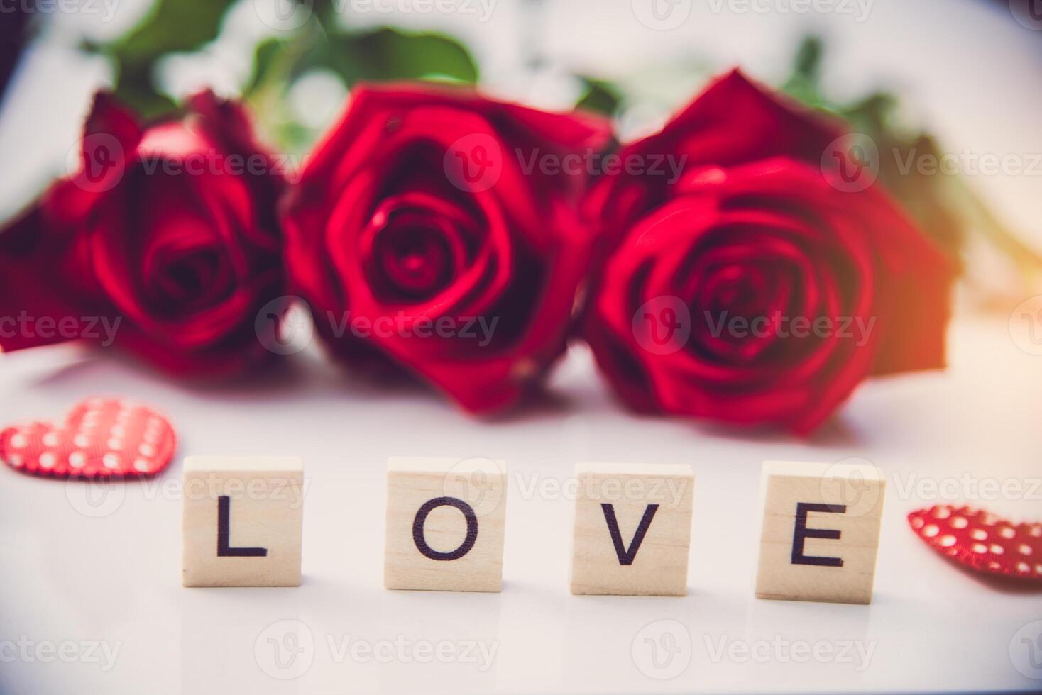 The red roses are placed on a white background and the wooden letters lined the word love photo