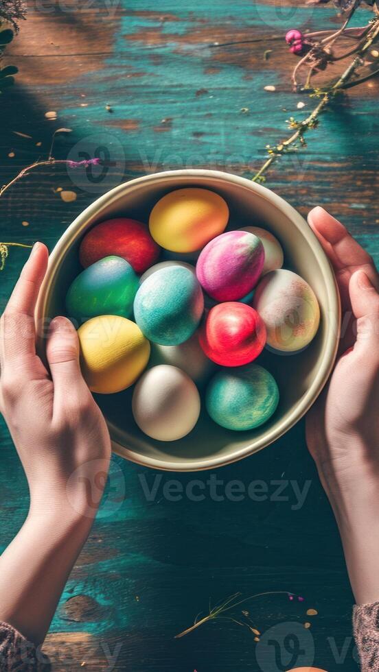 AI generated Hands holding a bowl filled with decorated Easter eggs, set against a green textured backdrop. Top view. Vertical format. Ideal For event planning, festive articles, and home photo