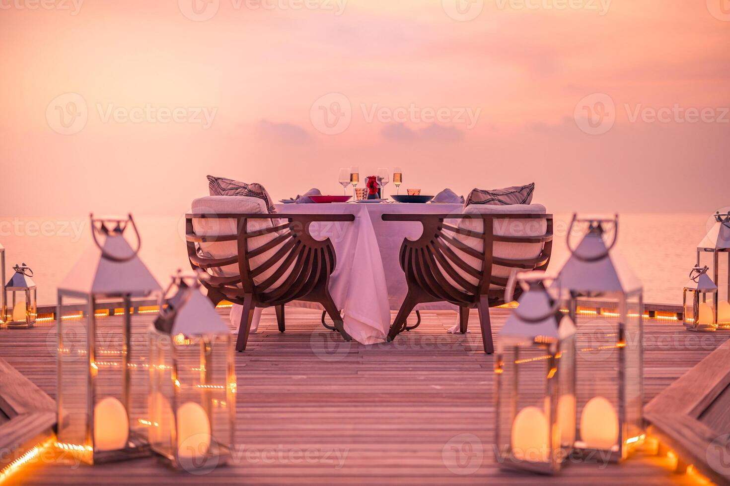 Amazing romantic dinner on the beach on wooden deck with candles under sunset sky. Romance and love, luxury destination dinning, exotic table setup with sea view photo