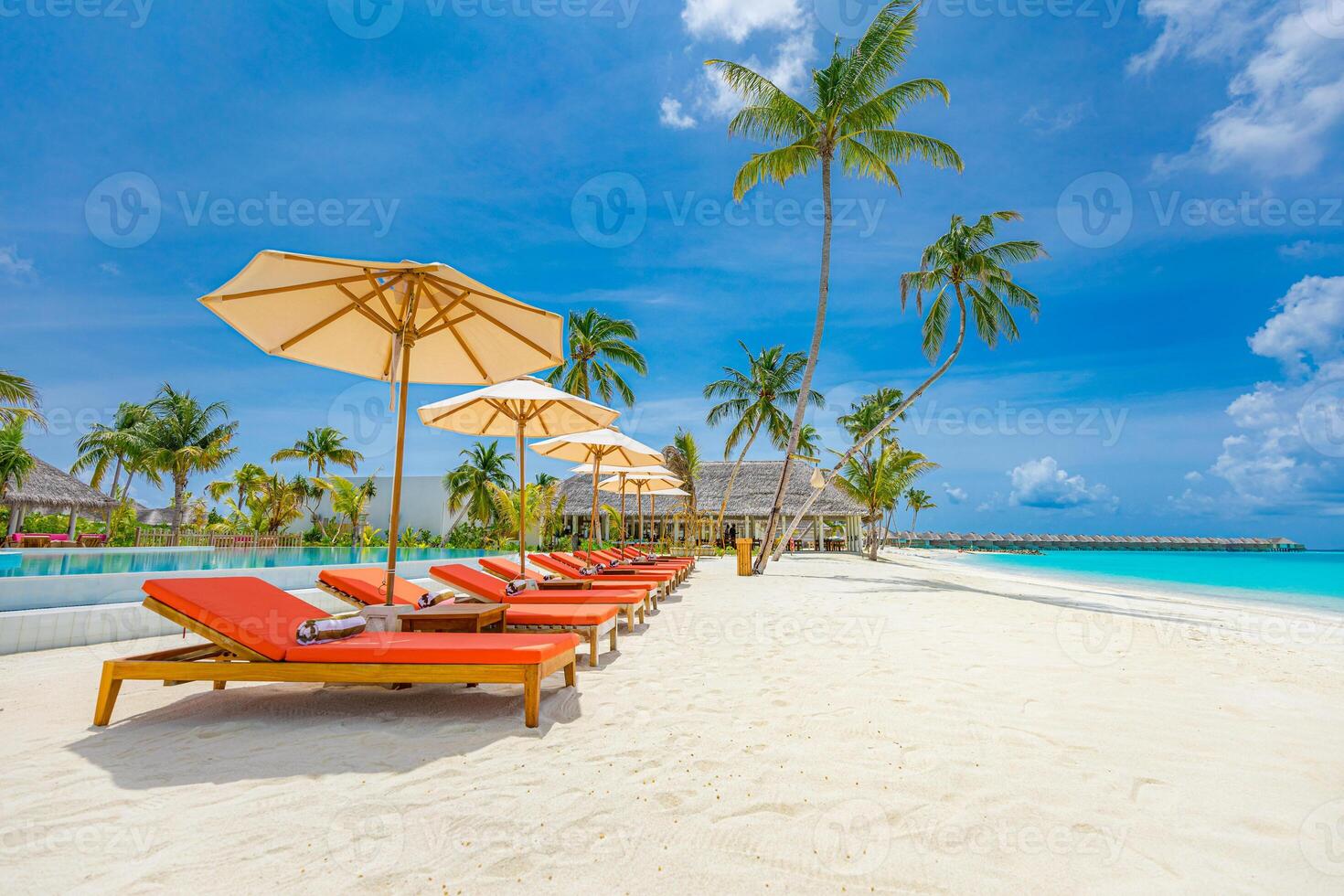 Panoramic holiday landscape. Luxury beach resort hotel. Leisure chairs loungers under umbrellas with palm trees, blue sunny sky. Stunning summer island seaside, travel vacation destination background photo