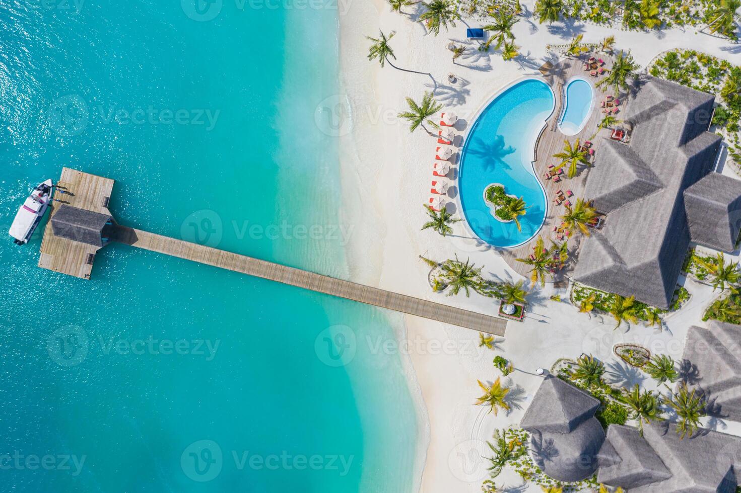 Beautiful aerial view of poolside and resort beach with wooden pier jetty. Luxurious tropical beach landscape, swimming, deck chairs and loungers, umbrellas. Tropical beach, aerial drone top view photo