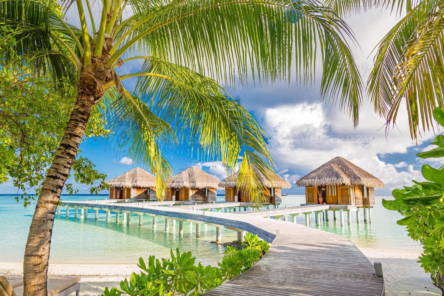 Luxury hotel with water villas and palm tree leaves over white sand, close to blue sea, seascape. Beach chairs, beds with white umbrellas. Summer vacation and holiday, beach resort on tropical island photo