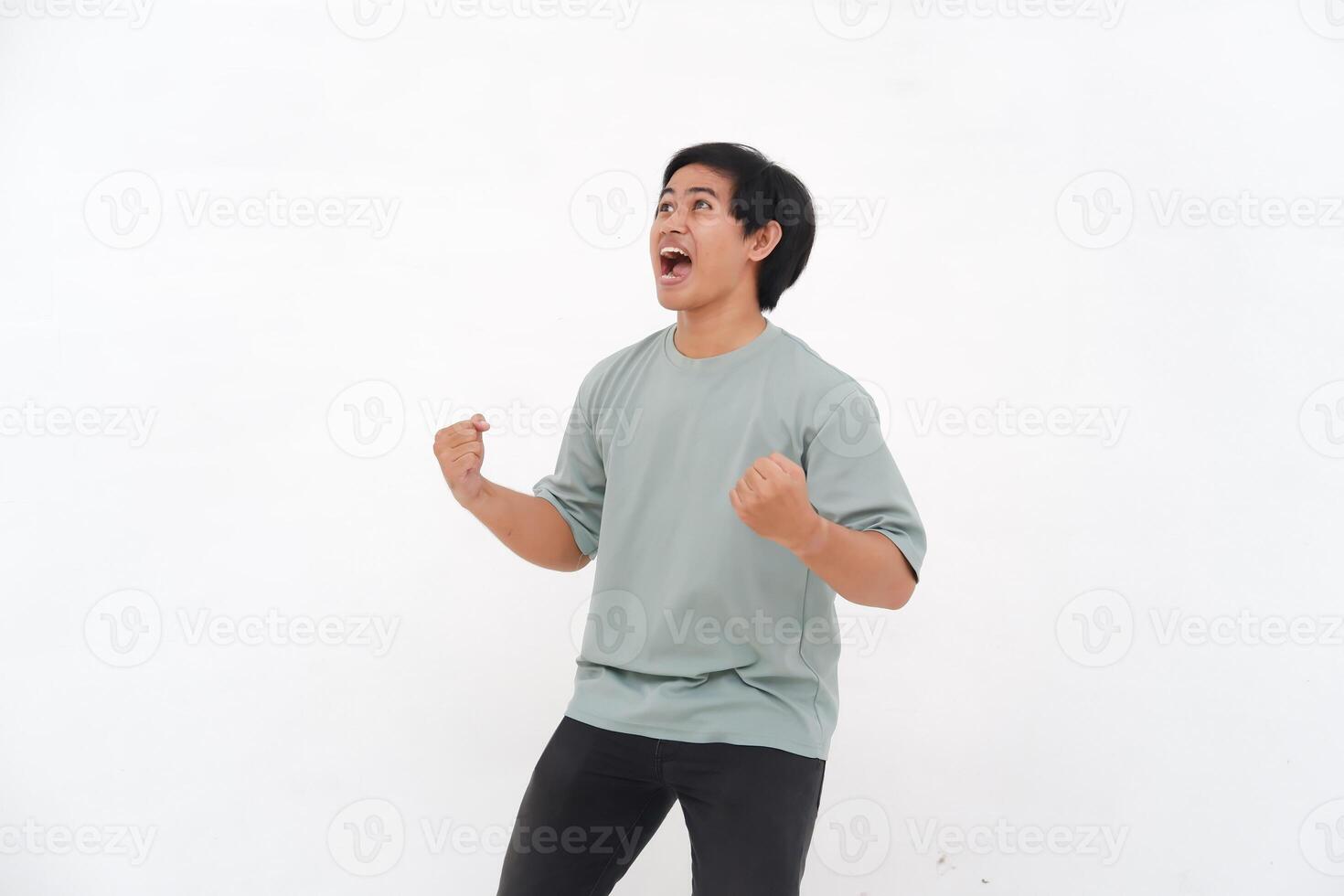 Young Asian man with an enthusiastic expression as if feeling victorious, depicting a sense of great satisfaction. photo