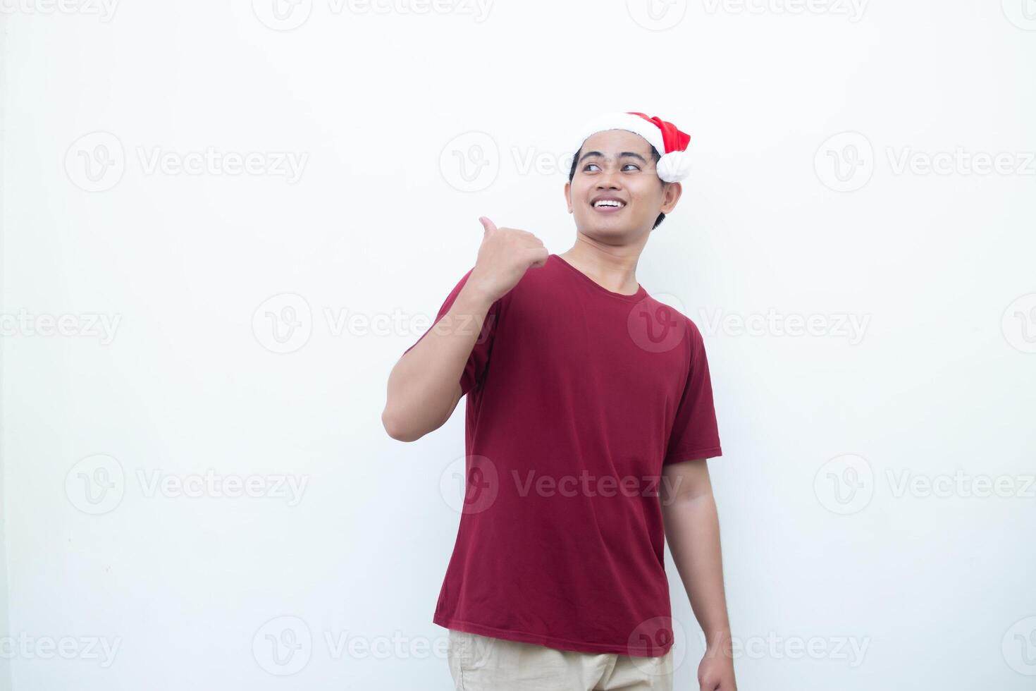 Young Asian man wearing a Santa Claus hat smiling, shock and pointing to her side isolated by white background for visual communication photo