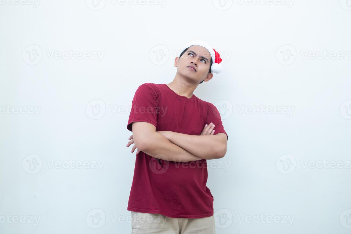 Young Asian man wearing a Santa Claus hat crossing his arms while smiling, shock and laughing with a white background for visual communication photo