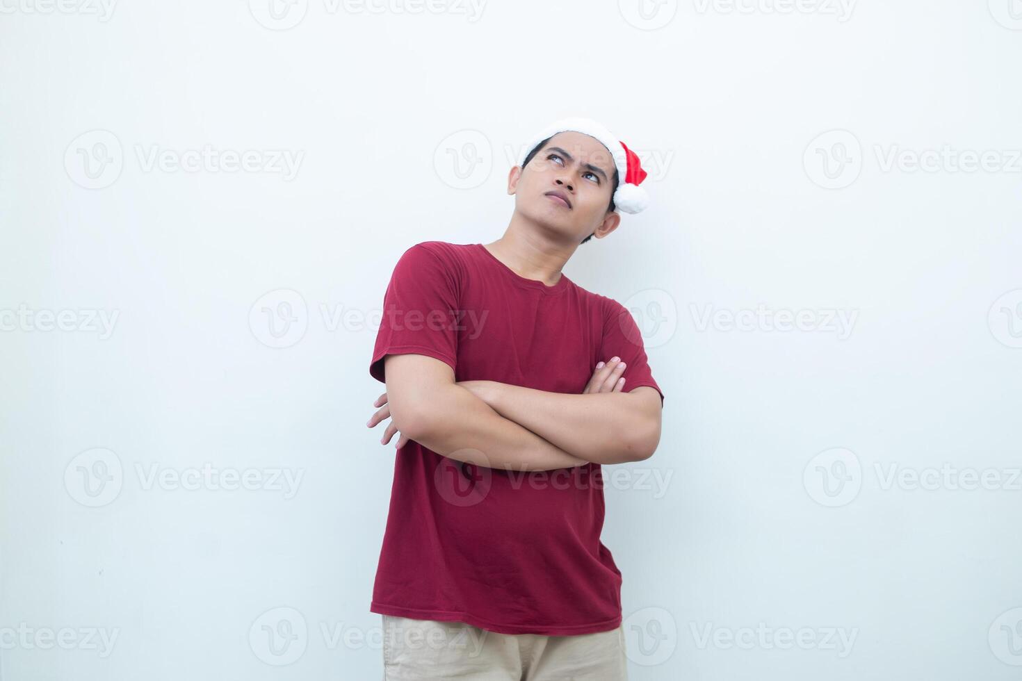 joven asiático hombre vistiendo un Papa Noel claus sombrero cruce su brazos mientras sonriente, conmoción y riendo con un blanco antecedentes para visual comunicación foto