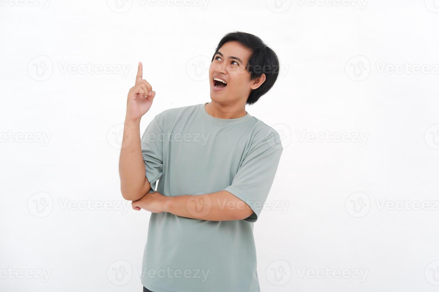 Excited Asian male employee wearing a tshirt pointing at the copy space above him, isolated by white background photo