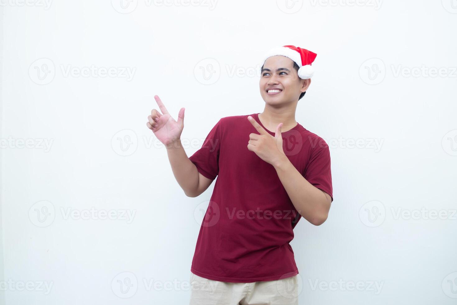 Young Asian man wearing a Santa Claus hat smiling, shock and pointing to her side isolated by white background for visual communication photo