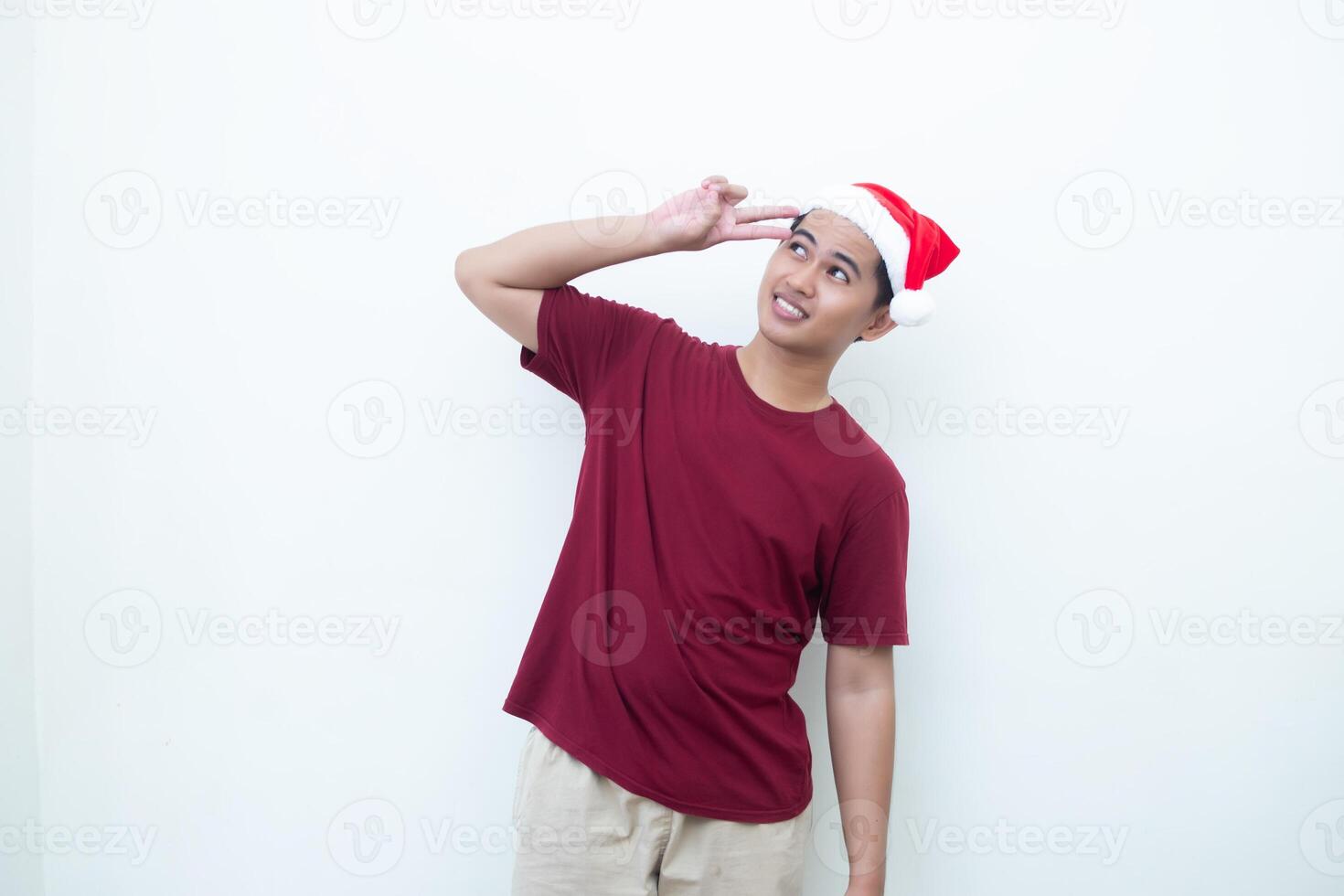 Young Asian man wearing a Santa Claus hat making a peace sign with 2 fingers isolated by a white background for visual communication photo